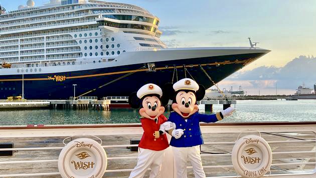 Captain Mickey Mouse and Captain Minnie Mouse in front of the Disney Wish cruise ship