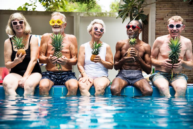 Group of seniors holding pineapples by a pool