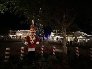 Tin soldier and other Christmas decorations at night in from of tall lit Christmas tree at Walt Disney World Resort's Magic Kingdom, with Cinderella Castle lit in the background.