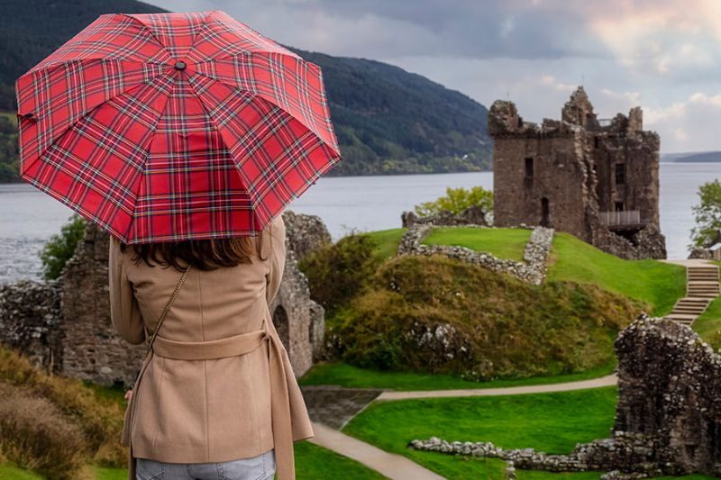 Woman holding an umbrella looking out over a castle in Scotland