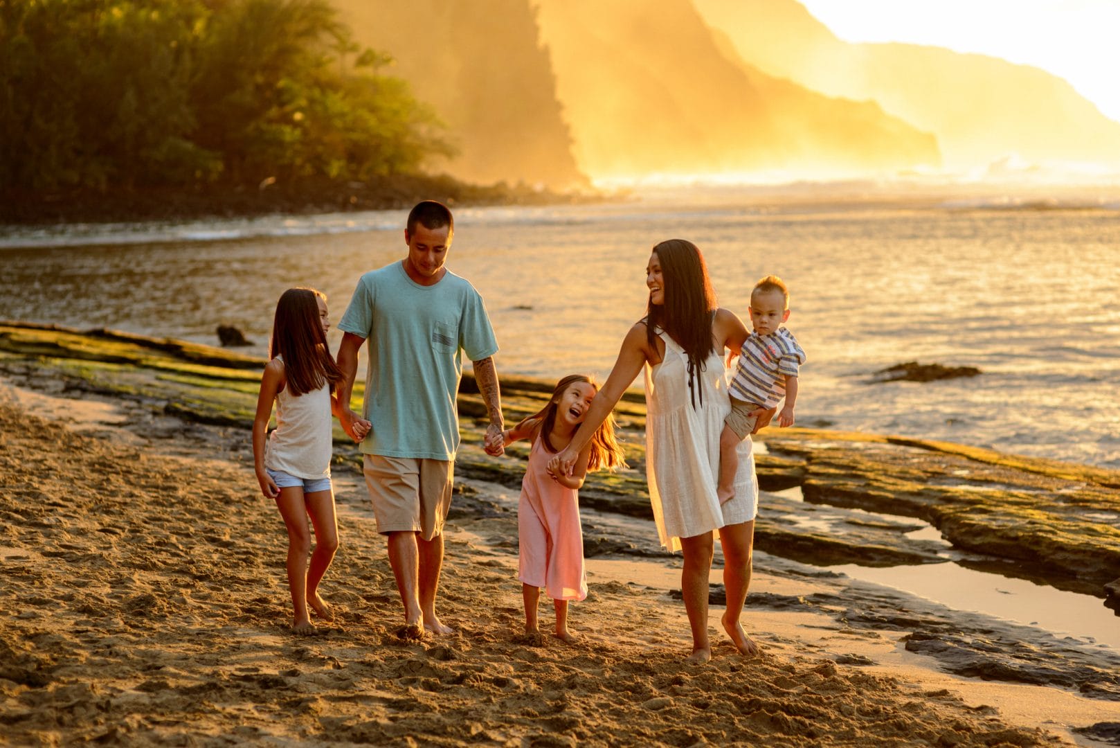 Sceptre Vacations. A beautiful family consisting of a Pacific Islander couple and their school age children walk on the beach together at sunset in Kauai, Hawaii.